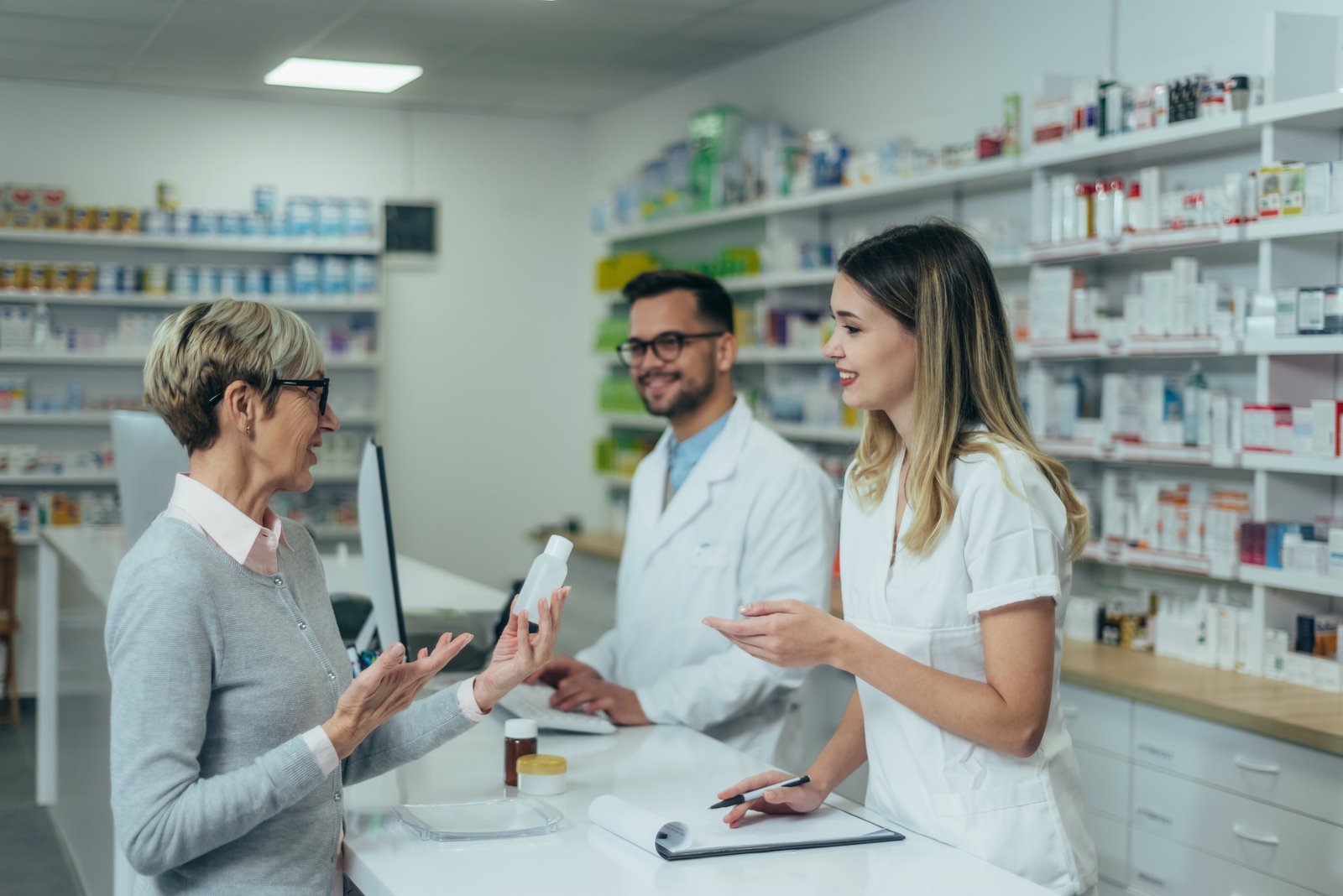 pharmacist-working-on-a-computer-while-female-pharmacist-is-giving-medications-to-senior-patient.jpg